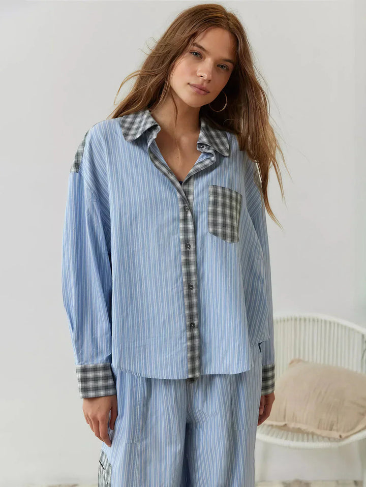 Woman wearing a light blue pajama set with plaid accents in a bedroom setting.